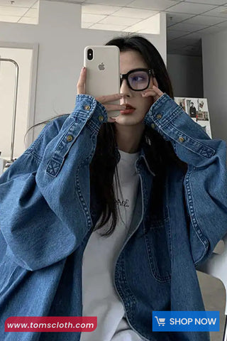 Person wearing a blue denim jacket and glasses, holding a phone with a visible brand logo.