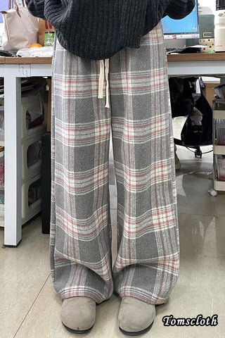 Person wearing plaid pants in an indoor setting with a desk and computer in the background.