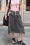 Person wearing a pink top and gray wide-leg pants standing on a sidewalk.