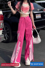 Person wearing a pink outfit with a white top and pink pants, standing in front of a car.