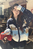 Woman wearing a decorative sweater with a snowy village design in an outdoor setting.