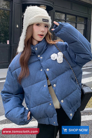 Woman wearing a blue puffer jacket and white fur hat on a street, with a visible brand logo.
