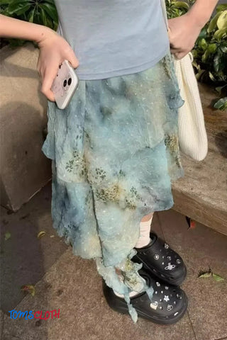 Person wearing a light blue floral skirt and black boots, holding a phone.