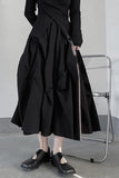 Person wearing a black dress with a large skirt and black shoes in a minimalistic setting.