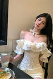 Woman in a white off-shoulder dress sitting at a table with a drink and food.
