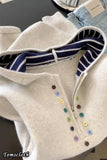 Close-up of a white garment with colorful buttons and striped trim on a dark surface.