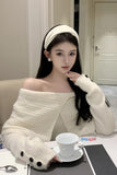 Woman in a white off-shoulder sweater sitting at a table with a cup.