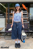 Person wearing a denim outfit with wide-leg pants and a blue cap, standing in front of a store with 'Good' signage.