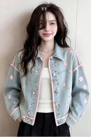 Woman wearing a light blue denim jacket with floral embroidery against a plain background