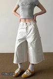 Person wearing a gray crop top and white wide-leg pants with a plain background
