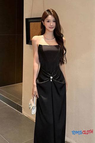 Woman in a black dress standing indoors with 'TOMS CLOTH' branding.