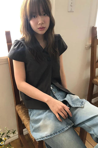 Person sitting on a wooden chair wearing a black top and light blue jeans.