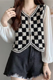 Person wearing a black and white checkered vest over a white blouse and dark shorts.