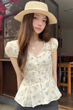 Woman wearing a floral blouse and wide-brimmed hat indoors.