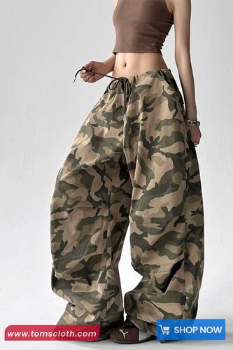 Camouflage pants worn by a person on a white background with 'tomscloth.com' branding.