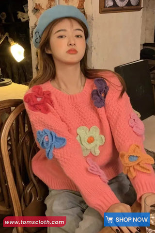 Woman wearing a pink sweater with floral patches in a casual setting.