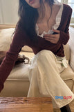 Person sitting on a couch wearing a brown cardigan over a white top and beige pants, with 'TOMS CLOTH' branding visible.