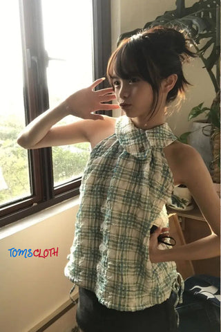 Woman wearing a green plaid top in a room with a window and plant.