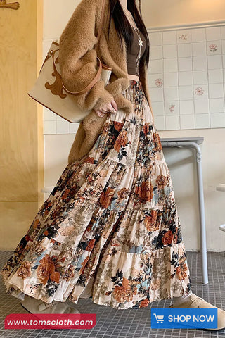 Person wearing a floral dress with a beige coat and holding a beige handbag in an indoor setting.