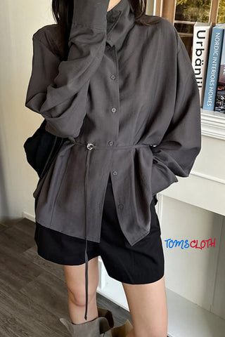 Person wearing a dark gray oversized shirt with a belt, standing indoors.