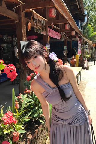 Woman in a gray dress standing in front of a traditional-style building with flowers and plants around.