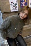 Person wearing a gray jacket standing in front of a textured wall with posters.