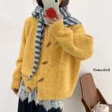 Person wearing a yellow cardigan with a striped scarf, holding a phone with a red case.