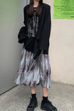 Person wearing a black jacket, patterned shirt, and pleated skirt against a plain wall.