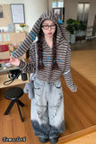 Person wearing a textured gray hoodie and ripped jeans in an indoor setting.