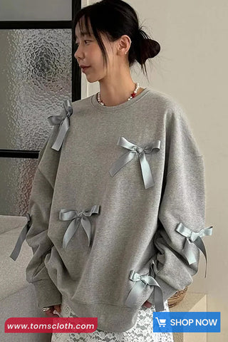 Woman wearing a gray sweatshirt with ribbons, standing indoors.