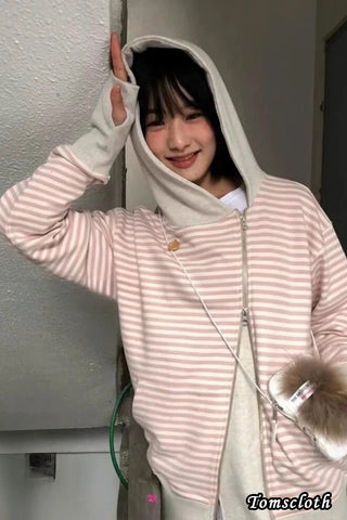 Person wearing a pink and white striped hoodie with a hood, standing indoors.