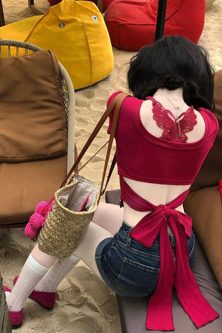 Person wearing a red bikini top with butterfly design and blue shorts, sitting on a chair.