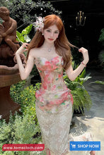 Woman in a floral dress standing outdoors with plants and a statue in the background