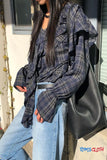 Person wearing a plaid shirt and jeans with a black bag, standing outdoors.