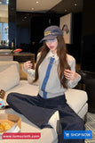 Woman sitting on a couch wearing a blue cap and suspenders, with a visible brand logo in the background.