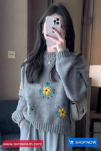 Person wearing a gray sweater with floral patterns, taking a mirror selfie.