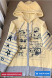 Yellow hoodie with cartoon designs on a brown surface, featuring the brand 'Toms Cloth'.