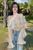Woman wearing a transparent off-shoulder top and blue jeans in a tropical setting