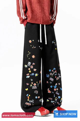 Black pants with colorful patterns worn by a person, with a red sweatshirt and red shoes on a white background.