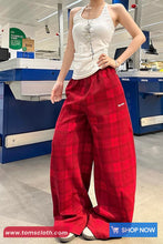 Person wearing a white sleeveless top and red plaid pants in a store setting.