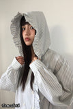 Person wearing a gray and white striped shirt with a hood against a plain background
