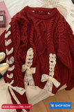 Red cable knit sweater with white lace bows on a bed