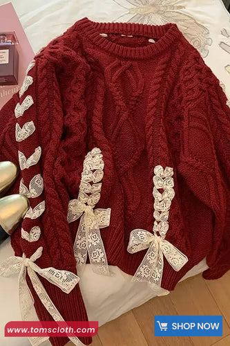 Red cable knit sweater with white lace bows on a bed