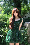 Woman in a green dress standing in a garden with trees and rocks in the background