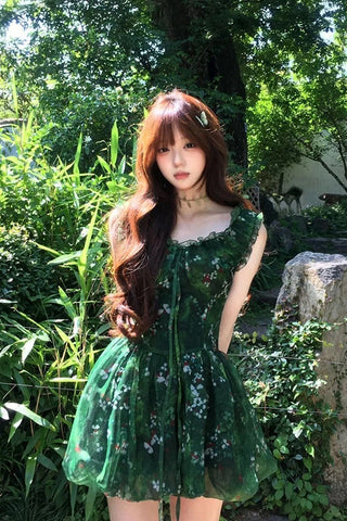 Woman in a green dress standing in a garden with trees and rocks in the background