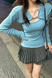 Person wearing a light blue sweater and pleated gray skirt on a sidewalk.
