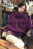 Woman wearing a purple sweater sitting on a wooden chair in a room with books and decor.
