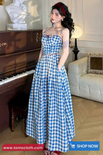 Woman in a blue checkered dress standing in a room with a piano and white sofa.