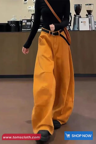 Person wearing mustard yellow pants and a black top in a store setting with 'Toms Cloth' branding.