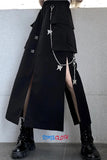 Person wearing a long black coat with star-shaped decorations and black boots against a light gray wall.